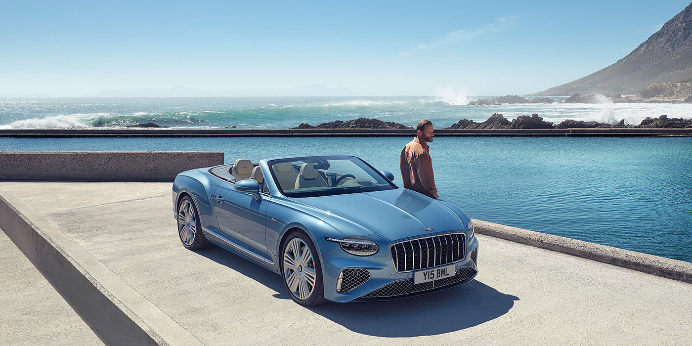 Bentley Manila New Bentley Continental GTC Azure convertible front view in Light Windsor blue paint with 22 inch ten spoke wheels parked by the sea in the sunshine
