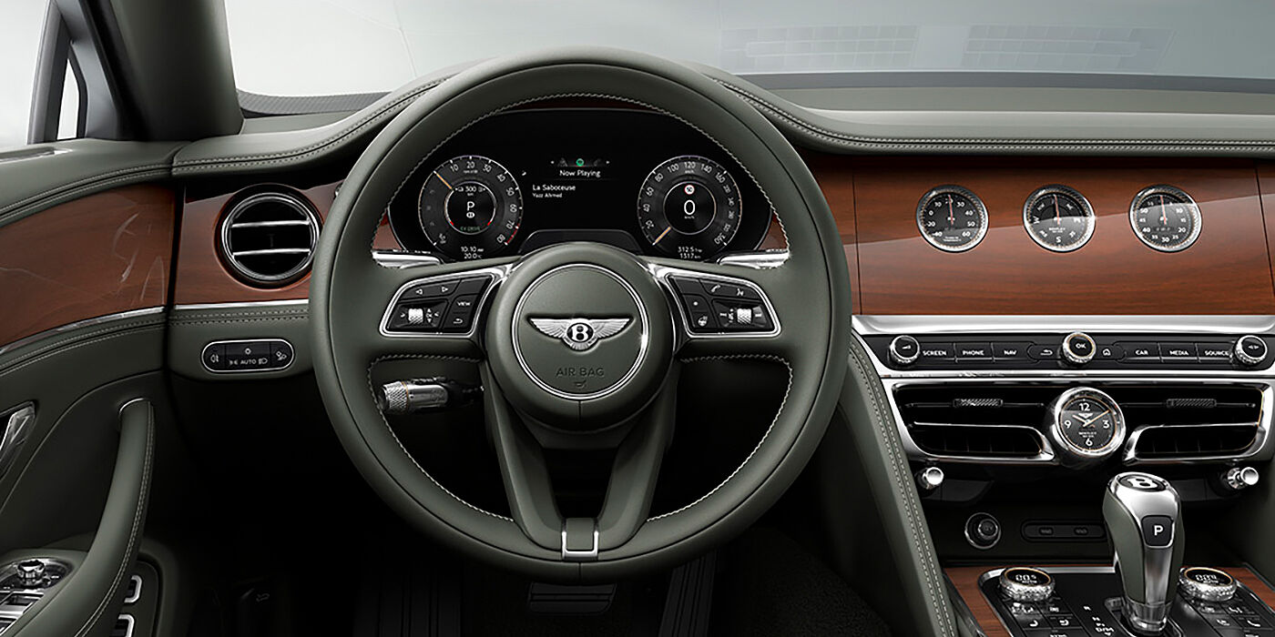 Bentley Manila New Bentley Flying Spur sedan front cabin in Cumbrian Green hide and Crown Cut walnut veneer showing steering wheel and Rotating Display with three clocks on face