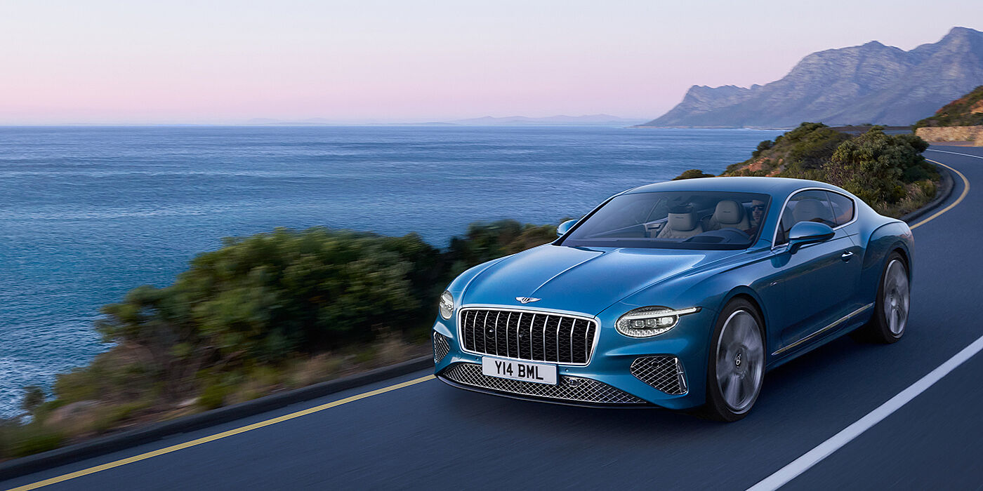 Bentley Manila New Bentley Continental GT Azure coupe in Light Windsor blue paint with 22 inch Azure wheels and chrome grill, driving dynamically by the sea