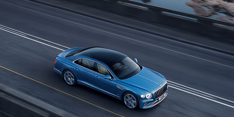 Bentley Manila New Bentley Flying Spur Azure sedan in Light windsor blue paint by Mulliner, with 22 inch Azure wheels seen from overhead driving dynamically on a country road