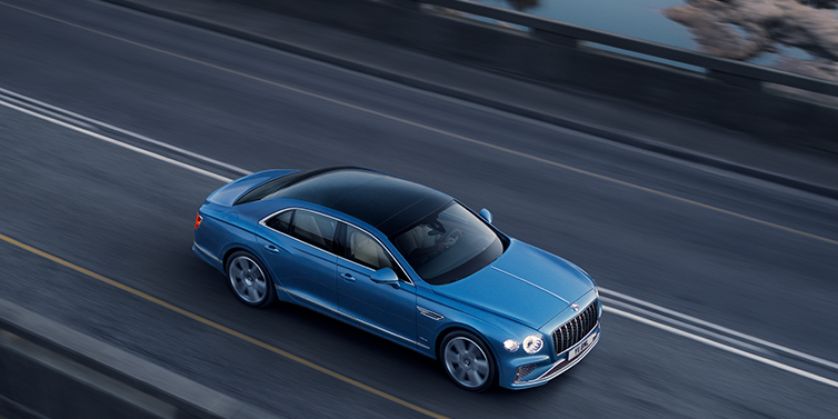 Bentley Manila New Bentley Flying Spur Azure sedan in Light windsor blue paint by Mulliner, with 22 inch Azure wheels seen from overhead driving dynamically on a country road