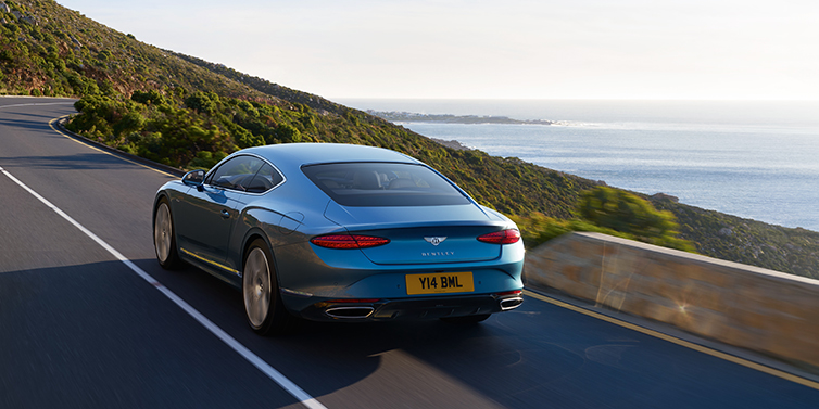 Bentley Manila New Bentley Continental GT Azure coupe in Light Windsor blue paint seen from the rear driving dynamically on a seaside road